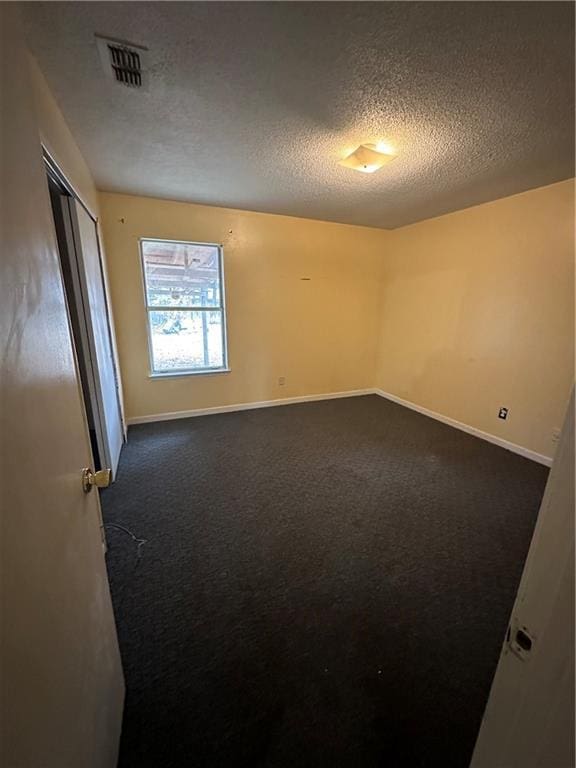 spare room with visible vents, dark carpet, a textured ceiling, and baseboards