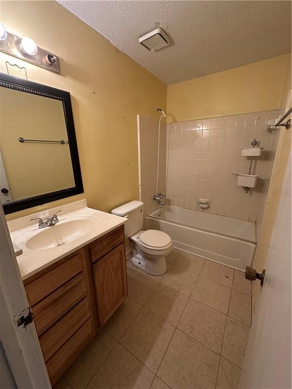 full bath with toilet, tile patterned floors, a textured ceiling, vanity, and washtub / shower combination