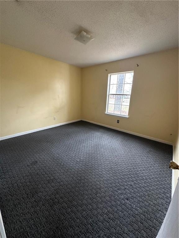 spare room with a textured ceiling, dark carpet, and baseboards