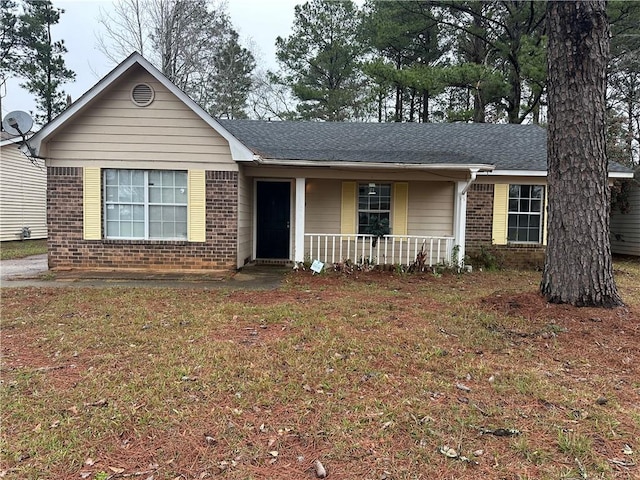 single story home featuring brick siding, a front yard, a porch, and a shingled roof