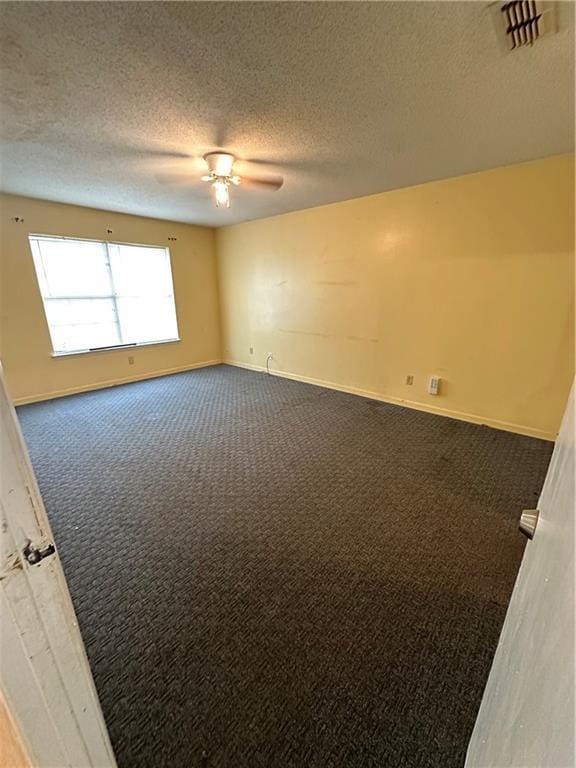 unfurnished room featuring a textured ceiling, visible vents, baseboards, a ceiling fan, and dark carpet