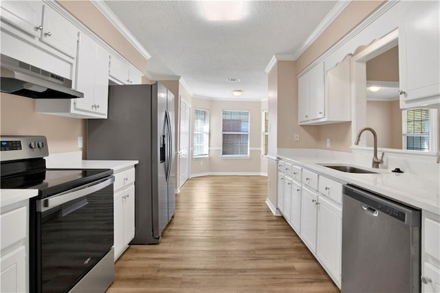 kitchen with crown molding, stainless steel appliances, light countertops, a sink, and under cabinet range hood