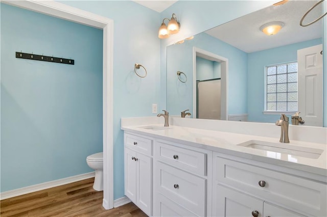 bathroom with wood finished floors, a sink, toilet, and double vanity