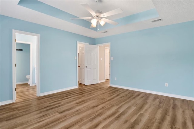 unfurnished bedroom featuring a tray ceiling, wood finished floors, visible vents, and baseboards