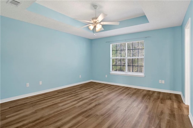 spare room with a tray ceiling, visible vents, baseboards, and wood finished floors