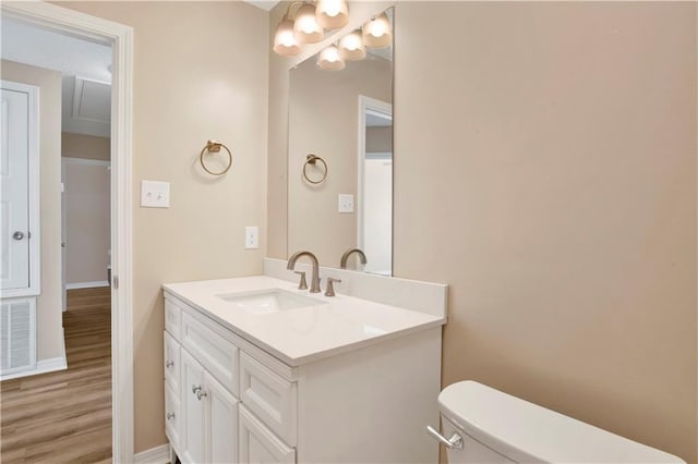 half bath with toilet, wood finished floors, vanity, visible vents, and baseboards