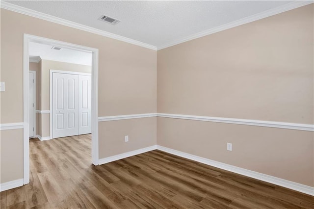 unfurnished room featuring baseboards, visible vents, wood finished floors, a textured ceiling, and crown molding