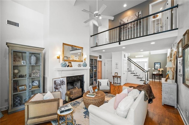 living room with a fireplace, wood-type flooring, a towering ceiling, and ceiling fan