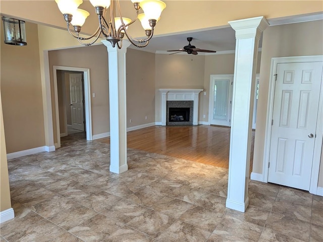 unfurnished living room with ceiling fan with notable chandelier, a premium fireplace, baseboards, decorative columns, and crown molding