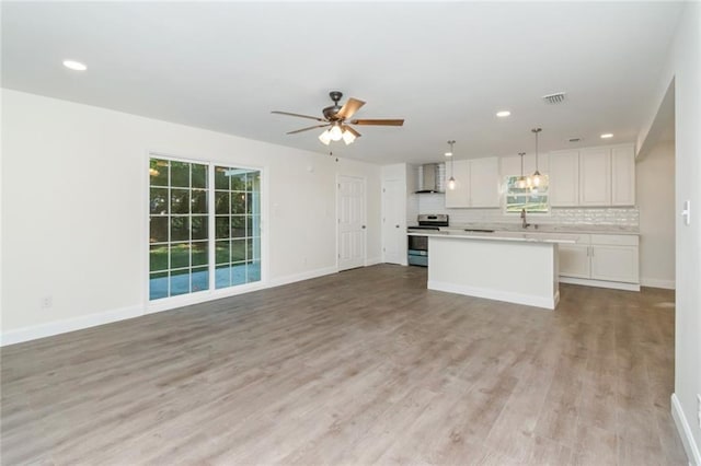 kitchen with wall chimney range hood, a center island, white cabinets, decorative light fixtures, and stainless steel range with electric cooktop