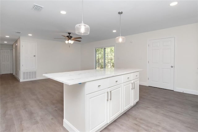 kitchen with hanging light fixtures, hardwood / wood-style floors, light stone counters, white cabinets, and a kitchen island