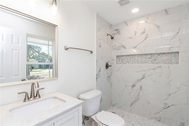 bathroom with tiled shower, vanity, and toilet