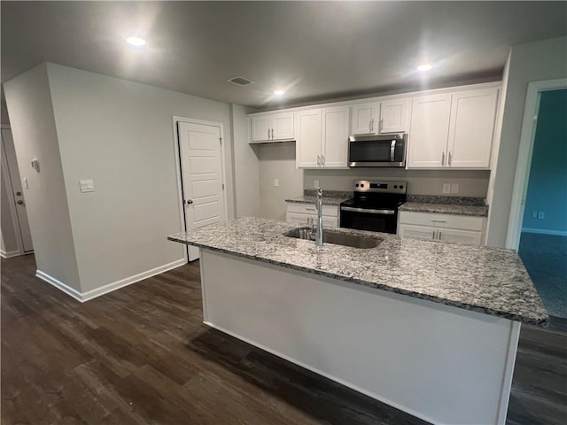 kitchen with stainless steel appliances, sink, white cabinets, light stone counters, and a kitchen island with sink