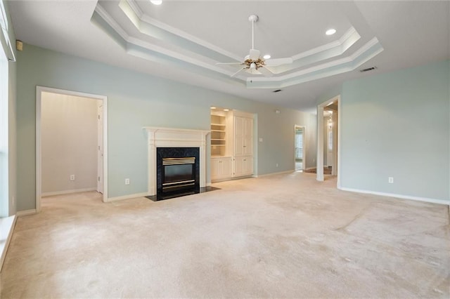 unfurnished living room featuring ornamental molding, light colored carpet, ceiling fan, a high end fireplace, and a raised ceiling