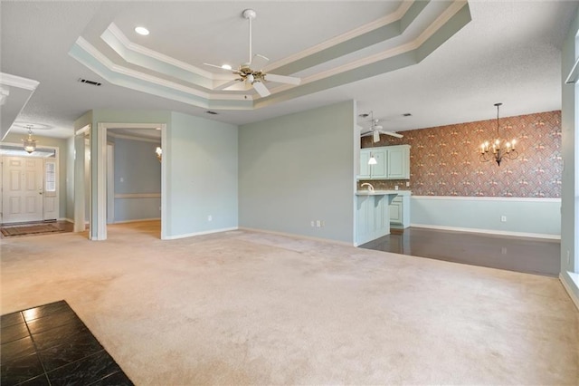 unfurnished living room with crown molding, a raised ceiling, ceiling fan with notable chandelier, and carpet