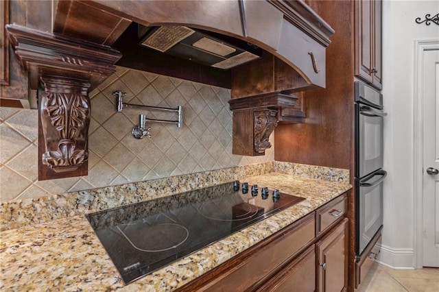 kitchen with backsplash, light tile patterned floors, light stone counters, and black appliances