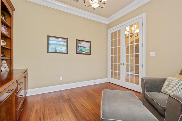 living area with baseboards, wood finished floors, a notable chandelier, and crown molding
