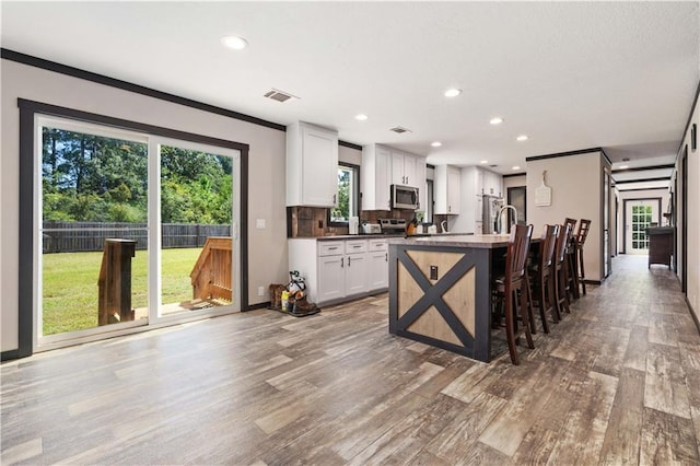 kitchen with a breakfast bar, a healthy amount of sunlight, hardwood / wood-style flooring, and white cabinets