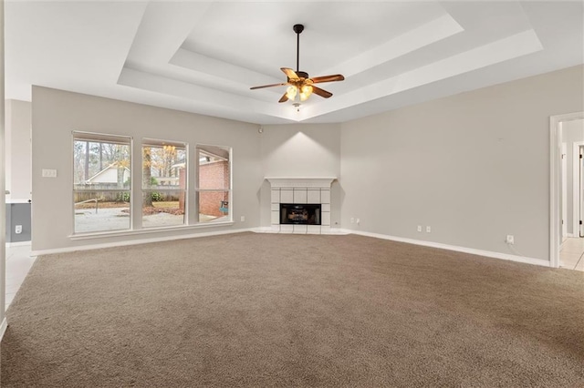 unfurnished living room with a tiled fireplace, light colored carpet, and a raised ceiling