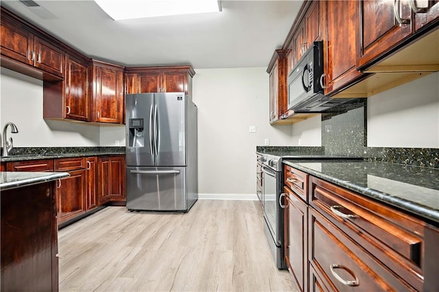 kitchen with black appliances, light wood-style floors, dark stone countertops, and baseboards