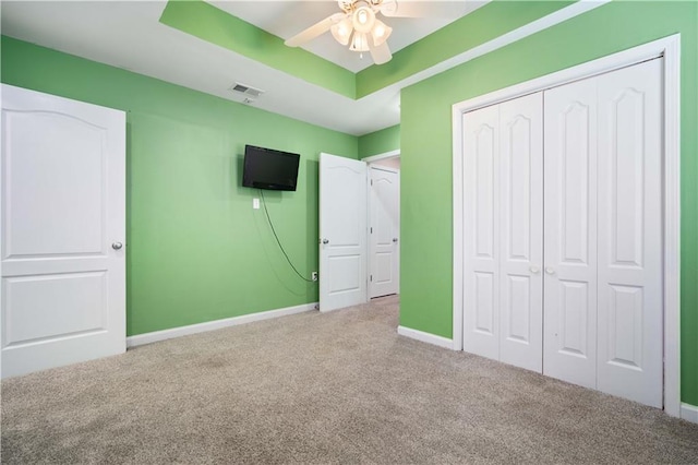 unfurnished bedroom with light colored carpet, ceiling fan, a tray ceiling, and a closet