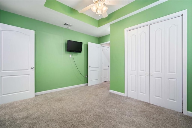 unfurnished bedroom featuring carpet flooring, a closet, baseboards, a tray ceiling, and ceiling fan
