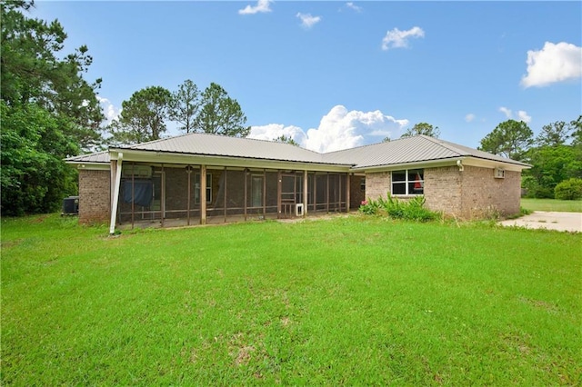 rear view of property with a sunroom, a lawn, metal roof, and brick siding