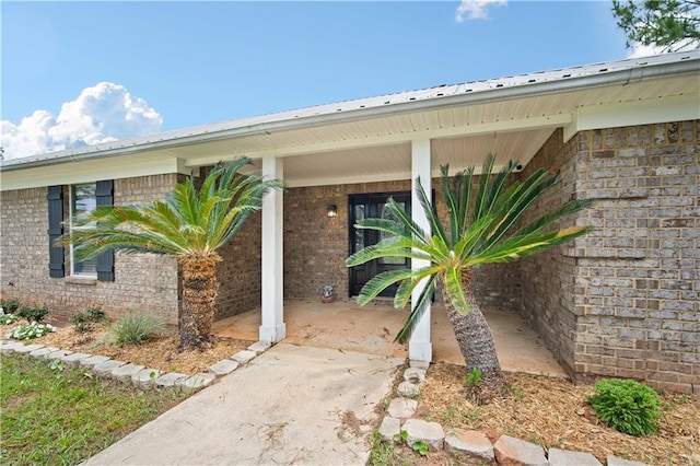 view of exterior entry with brick siding, metal roof, and covered porch