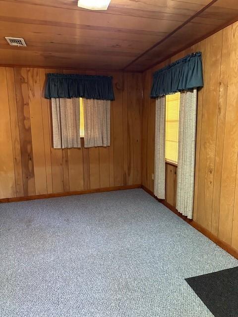 empty room with baseboards, visible vents, wood ceiling, and wooden walls