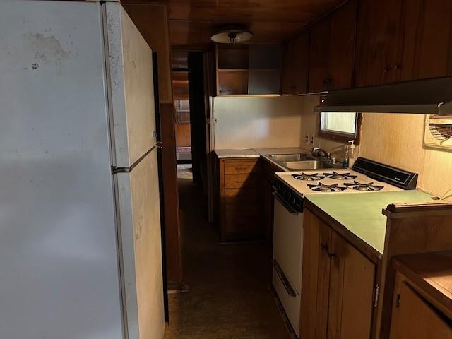 kitchen featuring freestanding refrigerator, a sink, light countertops, gas range oven, and under cabinet range hood