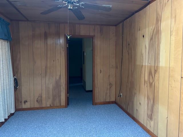 unfurnished room featuring wooden walls, a ceiling fan, and carpet floors