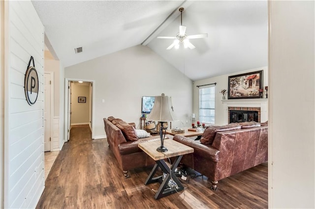 living room featuring lofted ceiling with beams, a brick fireplace, wood finished floors, and a ceiling fan