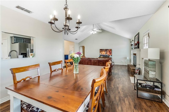 dining area with visible vents, a fireplace with raised hearth, dark wood-style floors, vaulted ceiling, and ceiling fan with notable chandelier