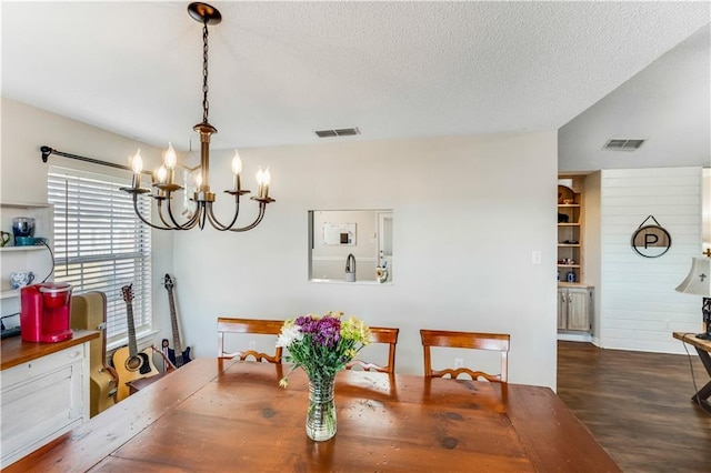 dining space with visible vents, a textured ceiling, an inviting chandelier, and wood finished floors