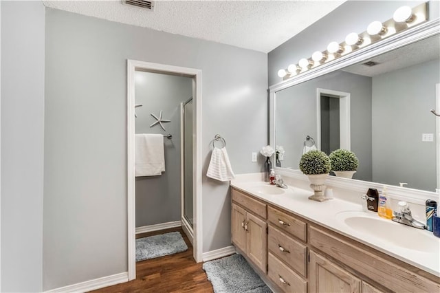 bathroom featuring a textured ceiling, wood finished floors, a sink, double vanity, and a stall shower