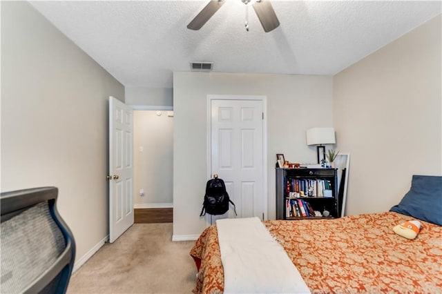 bedroom featuring ceiling fan, a textured ceiling, light colored carpet, visible vents, and baseboards