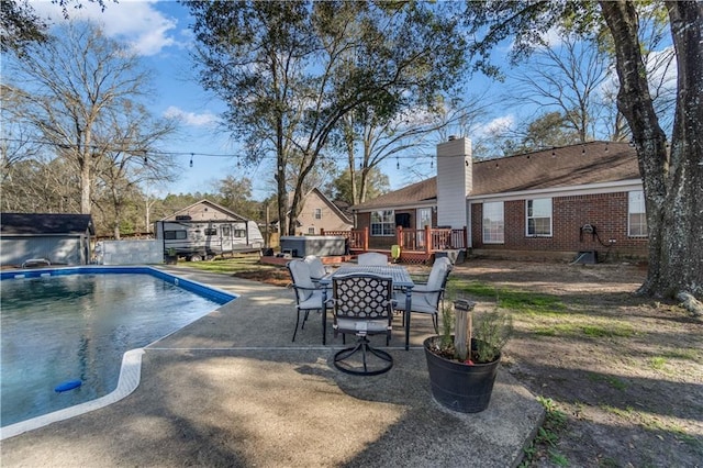 pool featuring a hot tub, a patio, an outbuilding, outdoor dining area, and a wooden deck