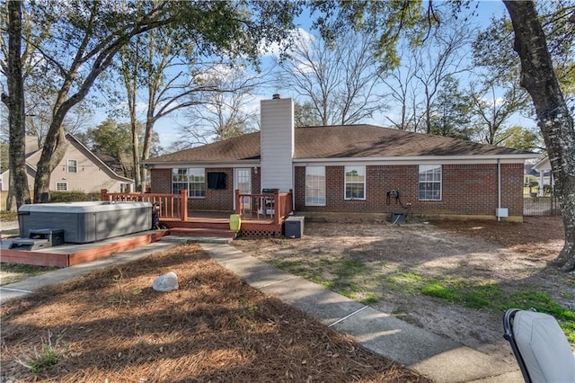 back of property with a chimney, brick siding, a hot tub, and a wooden deck