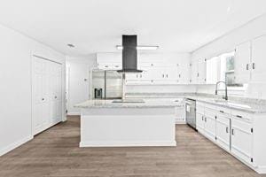 kitchen featuring appliances with stainless steel finishes, wall chimney range hood, wood-type flooring, white cabinets, and a kitchen island