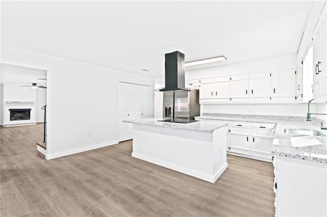 kitchen with island exhaust hood, sink, light hardwood / wood-style flooring, white cabinets, and a kitchen island