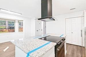 kitchen featuring wall chimney exhaust hood, dark wood-type flooring, stainless steel range oven, a center island, and white cabinetry