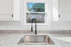 interior details with white cabinetry, light stone counters, and sink