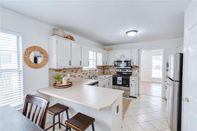 kitchen with stainless steel appliances, a peninsula, a sink, white cabinets, and light countertops