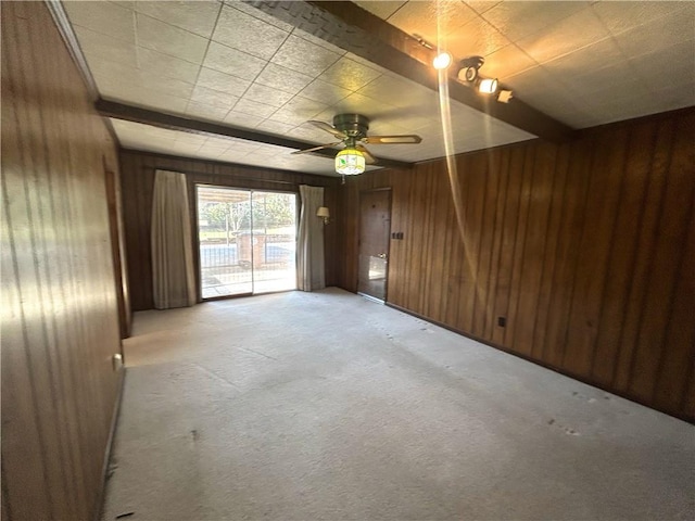 empty room featuring a ceiling fan, light carpet, wood walls, and beamed ceiling