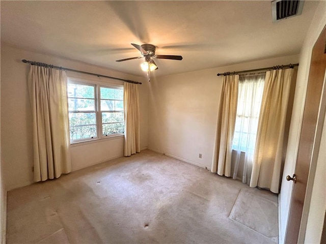 empty room featuring light colored carpet, visible vents, and ceiling fan