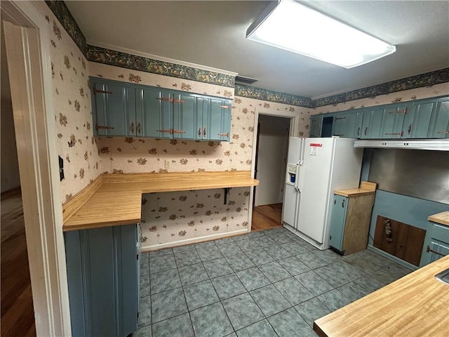 kitchen featuring wallpapered walls, butcher block counters, and white fridge with ice dispenser