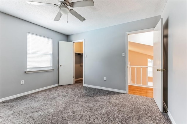 unfurnished bedroom featuring ceiling fan, a spacious closet, a textured ceiling, carpet floors, and a closet