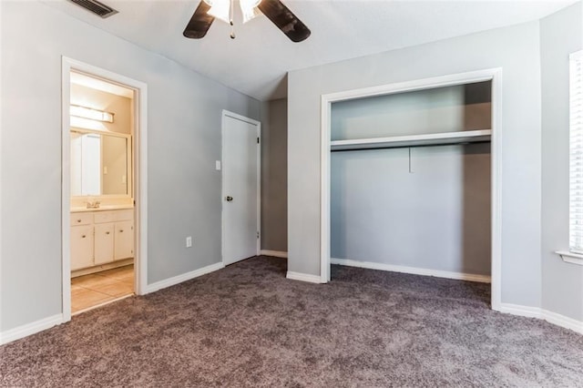 unfurnished bedroom with dark colored carpet, a closet, ensuite bath, and ceiling fan