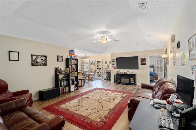 living area with visible vents, a ceiling fan, wood finished floors, a fireplace, and vaulted ceiling