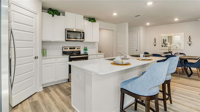 kitchen featuring light wood-type flooring, stainless steel appliances, sink, white cabinets, and an island with sink